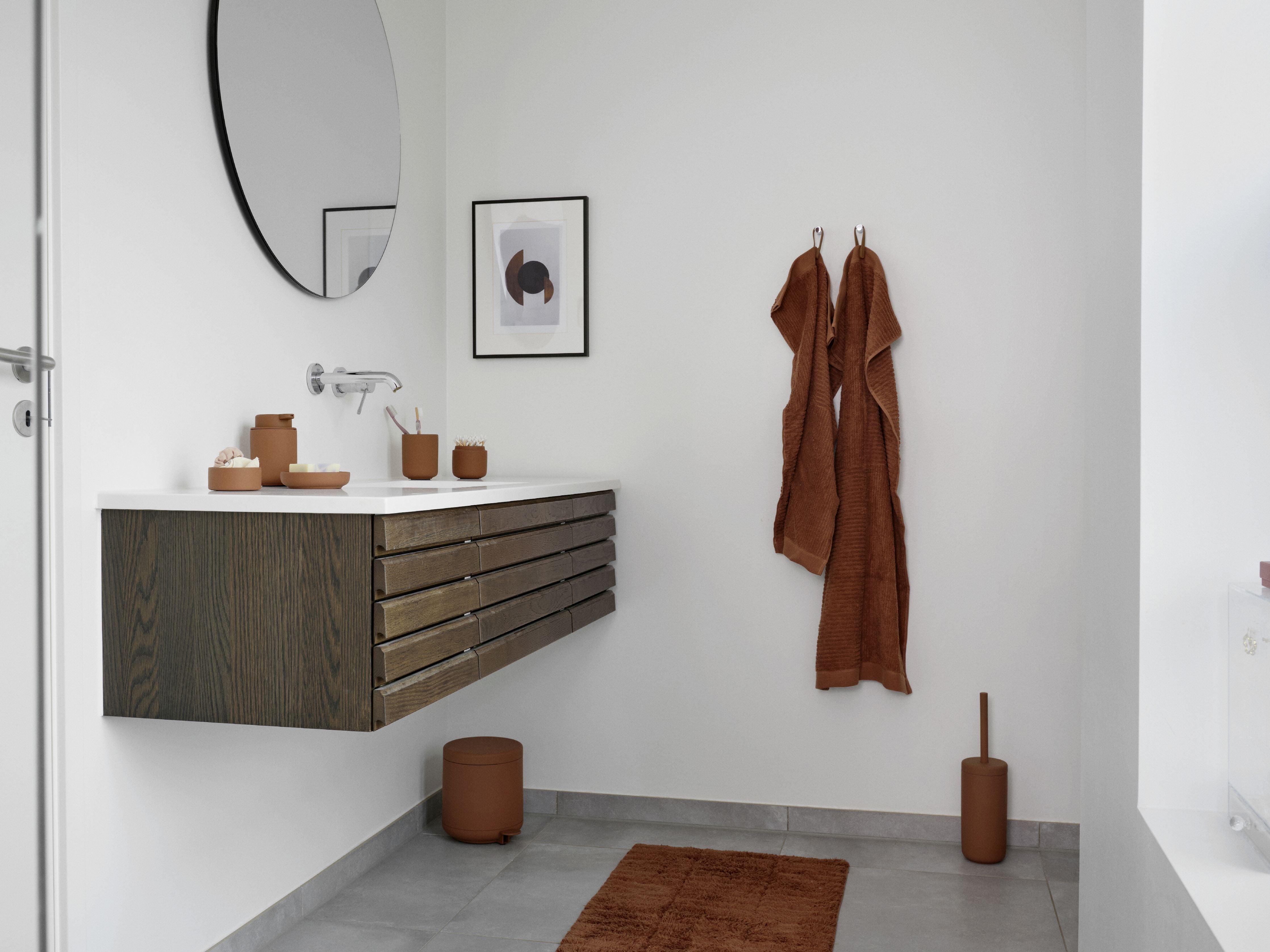 A white bathroom with brown towels, a Zone Denmark Ume Pedal Bin 4 Liter in terracotta, and a mirror.